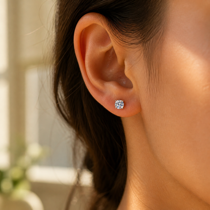 Four-prong round moissanite stud earring shown at a natural scale on the ear